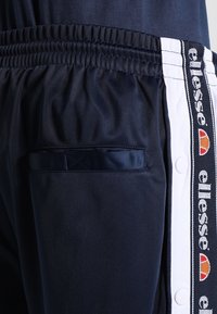 Marina byxor med struktur, elastisk midja och en sidremsa med tryckt logotyp. Inkluderar en liten fickdetalj.