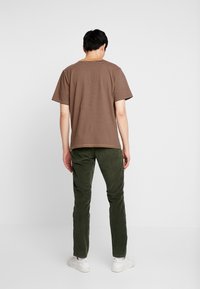 Brązowy pasiasty t-shirt z krótkim rękawem, noszony z zielonymi spodniami sztruksowymi. Charakteryzuje się luźnym krojem i okrągłym dekoltem. Buty są białe.