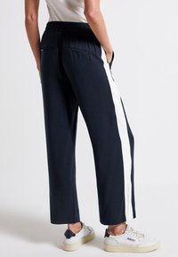 Marina blå byxor med en bred vit sidremsa, elastisk midja och fickor; tillverkade av mjukt tyg med rak bendesign.