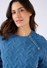 Blauwe kabelgebreide trui van gestructureerd garen met een ronde halslijn en drie decoratieve knopen op de linkerschouder.