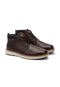 Brown leather ankle boots with a smooth texture, round toe, lace-up design, and contrasting beige rubber sole. Features stitching accents.