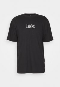 Camiseta negra de algodón con mangas cortas y cuello redondo. El texto en el frente dice "KING JAMES" en grandes letras blancas. Diseño simple y sin adornos.