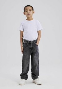 Witte t-shirt met korte mouwen, zwarte denim broek, relaxed fit, recht model, met zakken, gedragen met witte sneakers. Eenvoudige, casual outfit.