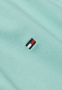 Tessuto testurizzato verde menta con un piccolo logo ricamato caratterizzato da strisce nere, rosse e bianche in una forma rettangolare.