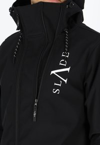 Schwarze Softshelljacke mit hohem Kragen, Reißverschluss vorne und Kordelzügen. Mit weißem "SLADE"-Logo auf der Brust und kontrastierenden Nähten.