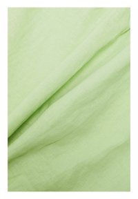 Tissu en lin vert clair avec une surface douce et texturée, présentant des plis subtils et un drapé, mettant en valeur une apparence lisse et naturelle.