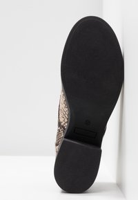 Chaussure à semelle plate en caoutchouc noir texturé, avec un dessus à motif serpent dans des tons beiges et bruns. Taille 37 indiquée.