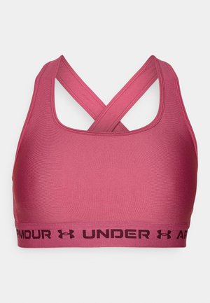 Rozā sporta krūšturis ar gludu tekstūru un krustveida siksnām. Apakšā ir melns elastīgs jostas ar "UNDER ARMOUR" zīmolu.