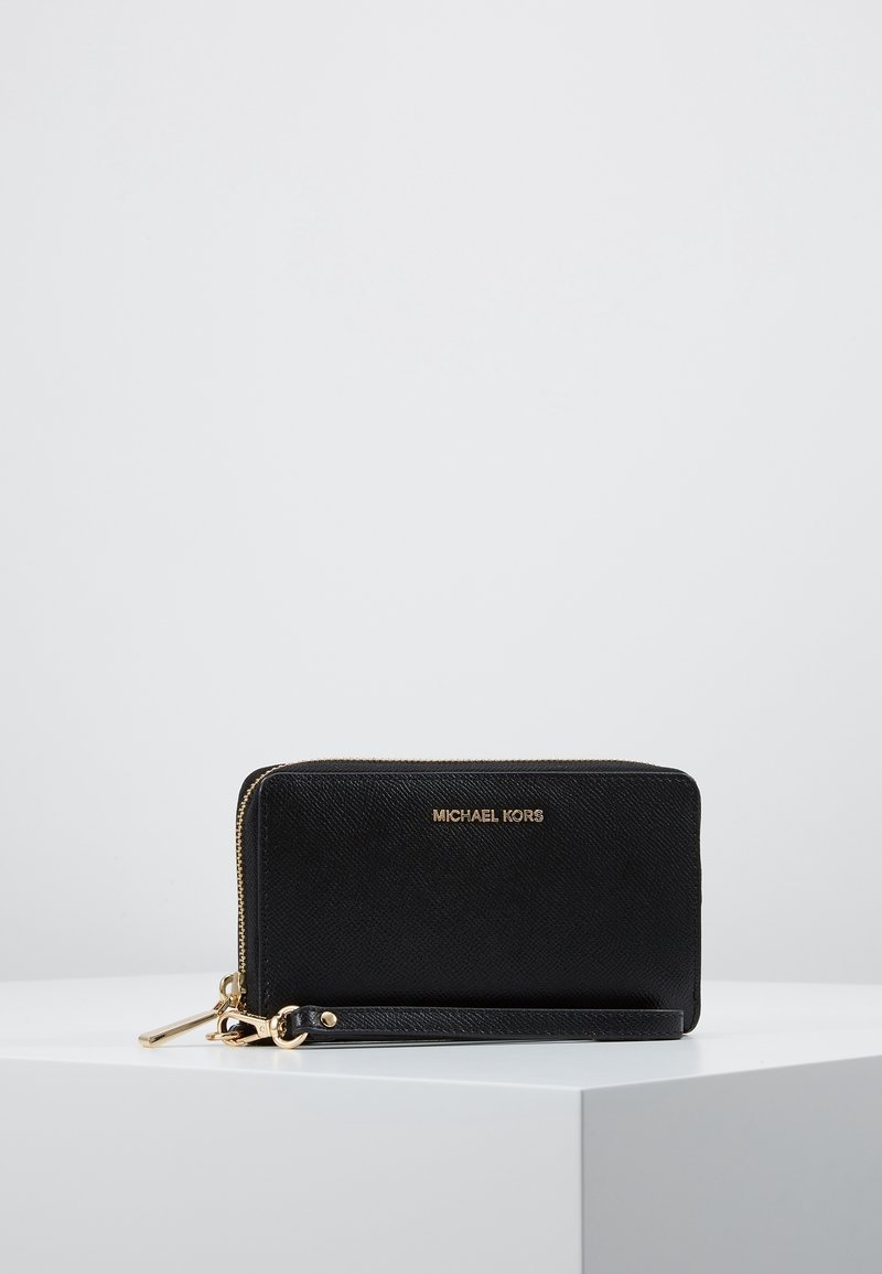 Portefeuille bracelet noir Michael Kors avec fermeture éclair dorée et logo, présenté sur une surface blanche sur fond gris clair.