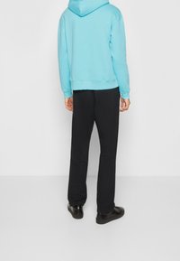 Jasnoniebieska bluza z kapturem i prążkowanym wykończeniem, zestawiona z czarnymi spodniami i czarnymi butami. Minimalistyczny design, jednolite kolory, gładka tekstura.