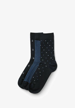 Schwarze Socken, darunter eine mit kleinen weißen Ankern, eine mit blauen Streifen und eine mit blauen Punkten, alle in unterschiedlichen Blautönen.