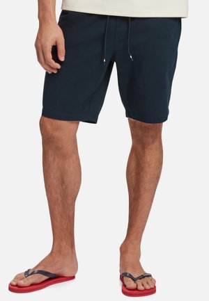 Marineblaue Badeshorts mit verstellbarem Bund und flachen Nähten, kombiniert mit schwarz-roten Flip-Flops mit einem strukturierten Riemen.