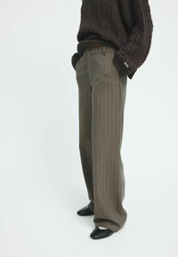 Un pantalon large à rayures brunes avec une texture lisse, complété par un pull en tricot foncé et des chaussures noires.