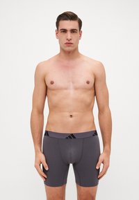 Boxer shorts cinzentos com uma cintura elástica preta e uma marca, apresentando um design justo e material de algodão suave. O estilo é de comprimento médio.