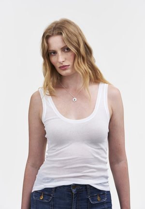 Top de tirantes blanco sin mangas con escote redondeado, hecho de una tela ligera. Combina con jeans de mezclilla azules con detalles en latón.