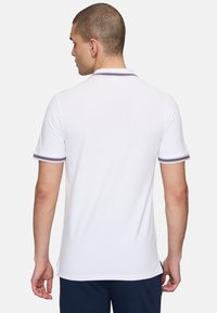 Vit polo-t-shirt med korta ärmar, med en klassisk krage och kontrasterande randig detalj vid ärmsluten. Minimalistisk design, mjuk textur.