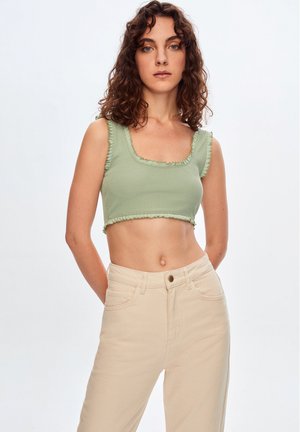 Top corto de canalé verde claro con escote cuadrado, adornos de volantes en los bordes, combinado con jeans beige de talle alto.