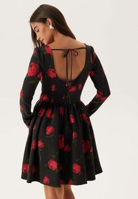 Abito nero con corpetto aderente, maniche lunghe e gonna svasata. Caratterizzato da stampe di rose rosse e una chiusura con nastro sul retro con scollatura profonda.