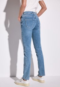 Vaqueros de color azul claro con corte ajustado, cinco bolsillos y cintura a media altura, que presentan una textura de denim suave y un diseño limpio y clásico.