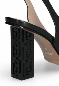 Juodos aukštakulnės sandalai su geometriniu blokiniu kulnu, išsiskiriančiu embosuotais raštais. Dirželiai yra lygūs, su nude spalvos vidiniu pamušalu. Elegantiškas dizainas.