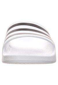Bílé skluzné sandály vyrobené z texturovaného plastu s třemi tenkými černými pruhy na pásku a plochou podrážkou.