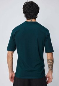 T-shirt à manches courtes en bleu sarcelle foncé, fabriqué dans un tissu léger et lisse. Doté d'un col rond et d'une coupe décontractée.