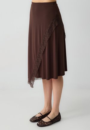 Bruine knielange rok van een glad materiaal, met een decoratieve kantversiering aan de zijkant. Gecombineerd met zwarte geweven ballerina's.