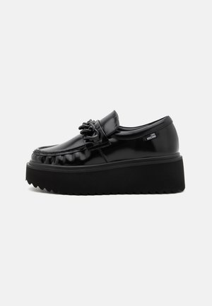 Scarpe con zeppa in pelle verniciata nera, con punta arrotondata, volant decorativi sulla parte anteriore e suola in gomma seghettata.