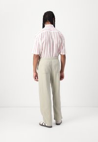 White short-sleeve shirt with red vertical stripes, paired with light green, loose-fitting trousers and black-and-white sandals.
