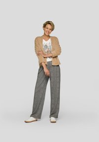 Beiger flauschiger Cardigan über einem weißen T-Shirt mit Grafik, kombiniert mit grauen karierten Schlaghosen und weißen Turnschuhen. Glatte, legere Kleidung.