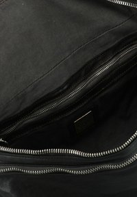 Interno di una borsa nera con una texture liscia, caratterizzato da scomparti con cerniera multipli e un piccolo etichetta del marchio. Tessuto durevole e design pulito.