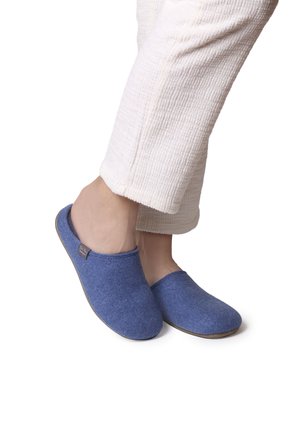 Zapatillas de casa azul de fieltro, con una forma redondeada y textura suave. Cuentan con una suela de color beige claro en contraste y una pequeña etiqueta de marca en el lateral.