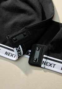 Czarne czapki z elastycznej tkaniny z płaskimi szwami i regulowanym czarnym zapięciem, z białą bandą z logo i czarnym napisem na podstawie.