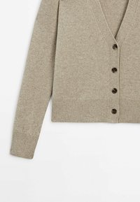 Cardigan en maille beige à manches longues, poignets et ourlet côtelés, col en V et quatre boutons foncés sur le devant.