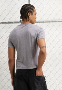 T-shirt gris à manches courtes au design ajusté, fabriqué en tissu doux, porté avec un short cargo noir déchiré présentant de grandes poches.