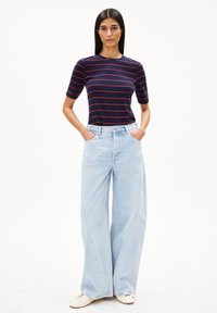Navy gestreiftes T-Shirt mit roten Linien, kombiniert mit hellblauen, weiten Jeans mit hoher Taille und Fünf-Taschen-Design. Getragen mit beigen Schuhen.