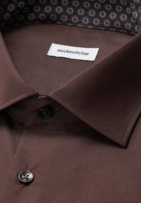 Donkerbruine shirt met een klassieke kraag, een enkele knoopsluiting en een gevoerde binnenkant met een patroon van cirkels in bruin en blauw.