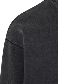 Felpa grigia scura con una texture morbida, vestibilità comoda e spalle scese. Il dettaglio delle cuciture a vista arricchisce il design minimalista.