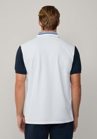 Polo senza maniche con schiena bianca, aperture blu per le braccia e colletto con dettagli a righe, realizzato in un tessuto leggero e liscio.