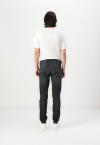Jeans negri din denim cu un design ajustat, buzunare la spate și o etichetă pe talie, asortați cu un tricou alb simplu.