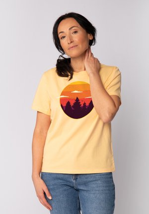 Geel katoenen T-shirt met een ronde grafische print van een zonsondergangsverloop en de silhouet van bomen in donkere kleuren. Korte mouwen en een relaxed fit.