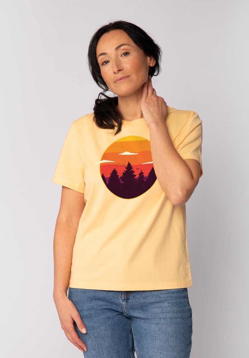 Geel katoenen T-shirt met een ronde grafische print van een zonsondergangsverloop en de silhouet van bomen in donkere kleuren. Korte mouwen en een relaxed fit.