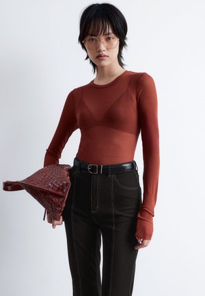 Long-sleeve rust-colored top with a fitted design, paired with black high-waisted pants featuring contrast stitching and a woven red handbag.