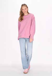 Felpa rosa con texture, scapoli scesi, look sovrapposto all'orlo, abbinata a jeans palazzo azzurri chiari e sneakers rosa.