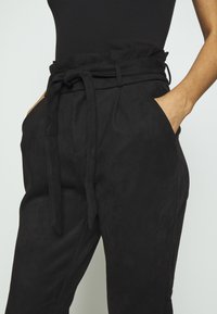 Svarta mockabyxor med hög midja, med ett knytbälte, sidofickor och en mjuk yta. Skräddarsydd passform med en elegant silhuett.