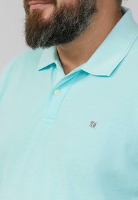 Lichtblauw poloshirt van textuurstof, met een twee-knopen sluiting en een klein logo op de linkerborst.