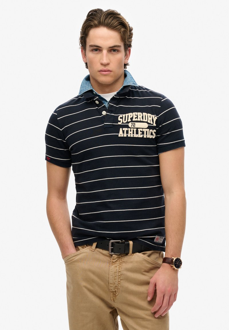 Marine gestreepte polo met een blauwe kraag, voorzien van een logo op de borst. Gecombineerd met kaki broek en een zwarte riem. Casual pasvorm en ontwerp.