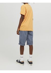 Oranje katoenen t-shirt, losse pasvorm, gecombineerd met blauw korte broek met opgerolde mouwen. Witte sokken met tekst en donkere sneakers met beige accenten.