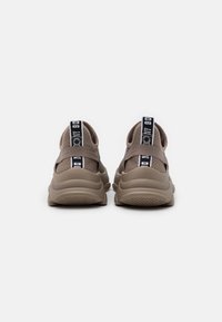 Sneakers in rete beige con fascetta elastica sul retro, suola testurizzata e linguetta sul tallone in bianco e nero con logo per ulteriore supporto.