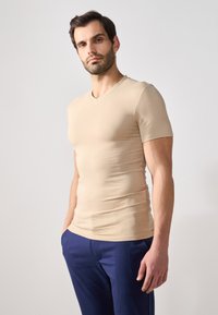 Tricou bej cu mânecă scurtă și decolteu în V, realizat dintr-un material elastic și neted, asortat cu pantaloni bleumarin. Siluetă simplă și aerodinamică.